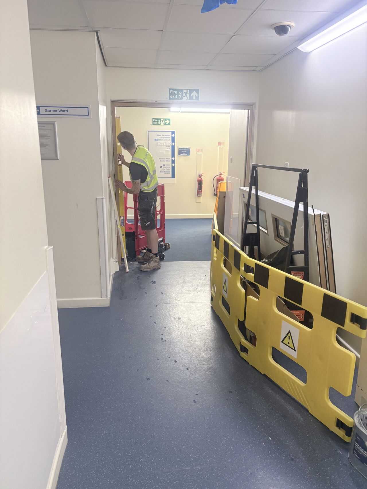 JFD installer checking a frame for plumb in a live hospital corridor, Bodmin