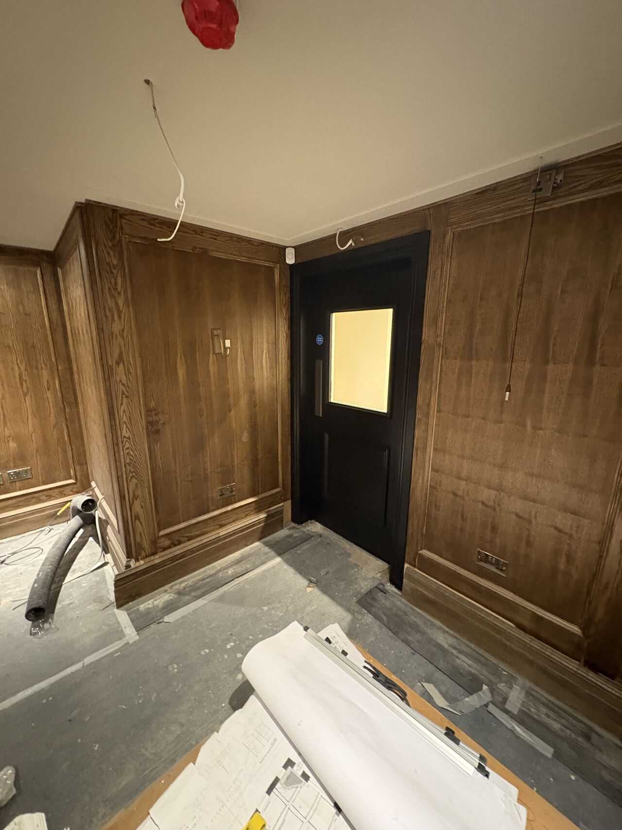 Existing opening mid-refurbishment: new doorset in a panelled wall with exposed ceiling cabling and floor ducting
